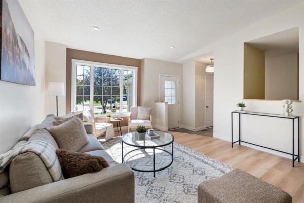Living room featuring a sectional sofa, round coffee table, patterned rug, and a large window with exterior view. - 11 Dufort Place, Winnipeg