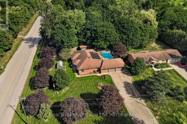 Aerial view of a brick ranch home surrounded by trees, featuring a swimming pool and solar panels. - 11 Elisabeth Street, East Zorra Tavistock