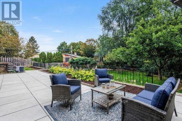 Backyard patio with wicker furniture overlooking a green lawn and garden. - 11 Fareham Crescent, Toronto