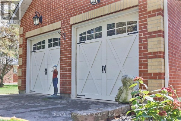 Close-up of two white garage doors with decorative windows and black hardware on a brick house. - 11 Fisher Drive, Adjala Tosorontio