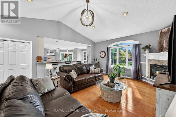 Living room with leather sofas, a stone fireplace, hardwood floors, and an open view to the kitchen. - 11 Fisher Drive, Adjala Tosorontio