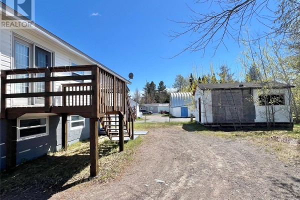 View of the backyard with a wooden deck, shed, and a large metal storage structure in the distance. - 11 Fourth Avenue, Badger