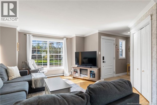 Living room with a grey sectional sofa, coffee table, and television in front of a large window. - 11 Gagnon Drive, Moncton