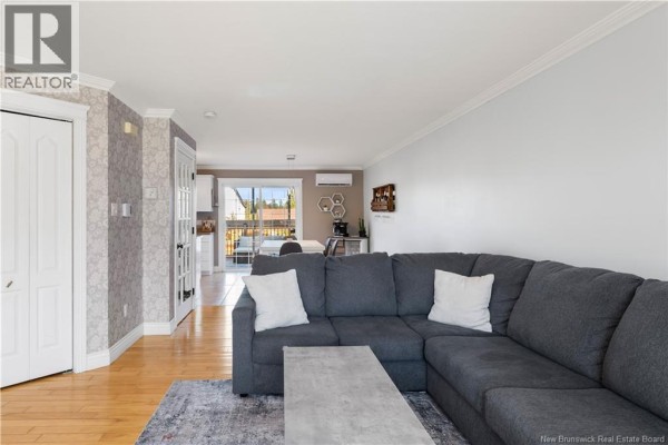 View of a living room sectional sofa looking towards a dining area and balcony access. - 11 Gagnon Drive, Moncton