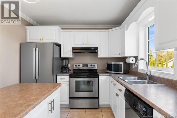 White kitchen cabinets, stainless steel appliances including a refrigerator, stove, and microwave, with a double sink. - 11 Gagnon Drive, Moncton