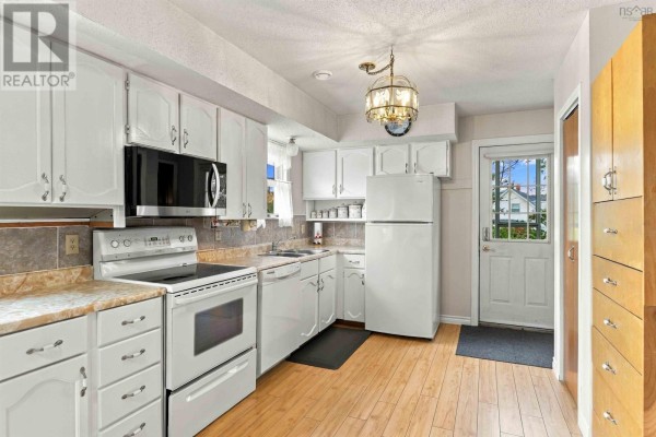 White kitchen with light wood floors, white cabinets, stainless steel appliances, and a door leading outside. - 11 Green Lane, Falmouth