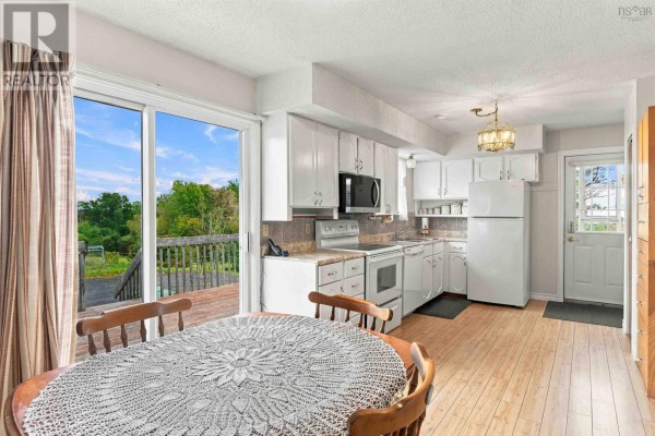 Dining area with a wooden table and chairs, looking into a white kitchen and out onto a deck. - 11 Green Lane, Falmouth
