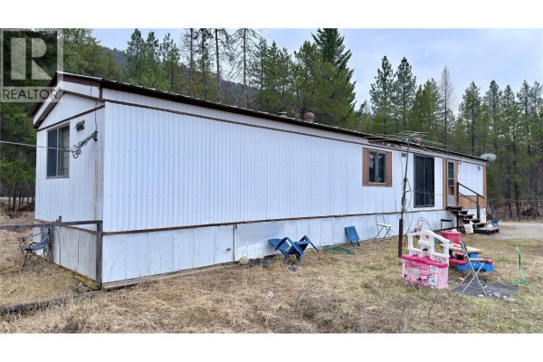 Dry grassy field surrounded by tall pine trees and wooden fence posts. - 11 Haggen Road, Beaverdell
