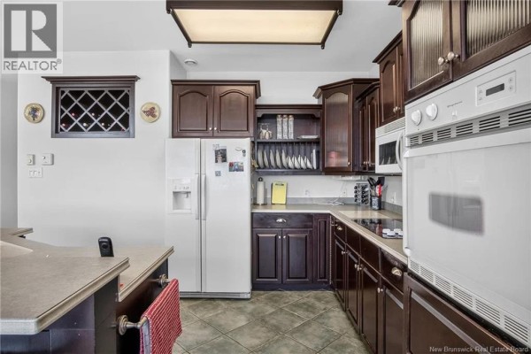 Kitchen with dark wood cabinets, white appliances, a wine rack, and tiled flooring. - 11 Harbour Terrace, Saint John