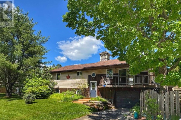Exterior of the house with a deck, garage, and mature trees in the yard. - 11 Harris Street, Muskoka Lakes