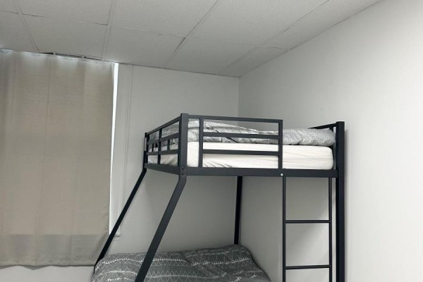 Bedroom with grey patterned bedding on black metal bunk beds and a window with light grey curtains. - 11 King Street E, Cobourg