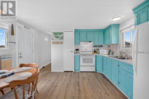 Kitchen and dining area with oval wood table, chairs, and turquoise cabinets, white appliances, and wood floors. - 11 Macfadyen, Augustine Cove