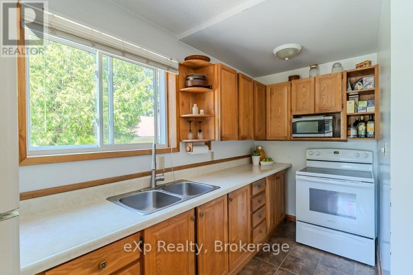 Kitchen counter with a double sink, wood cabinets, microwave, and a white oven below. - 11 Marigold Street, South Bruce Peninsula