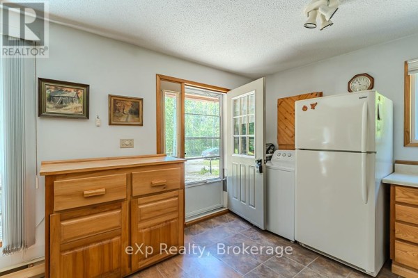Kitchen area with a white refrigerator, washing machine, wooden cabinet, and a glass-paned door. - 11 Marigold Street, South Bruce Peninsula
