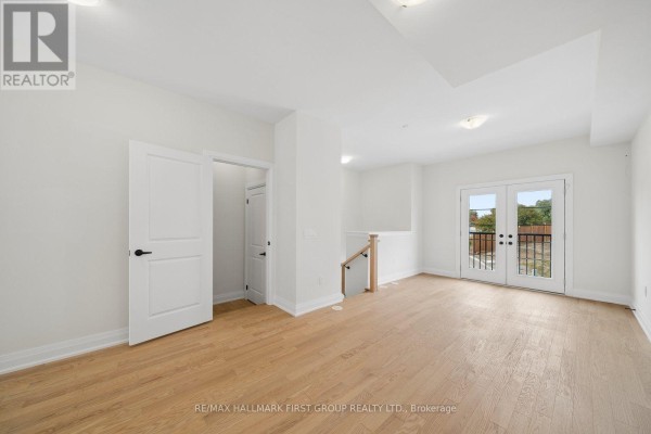 Empty room with light wood floors, white walls, and double glass doors leading to a balcony. - 11 Marret Lane, Clarington