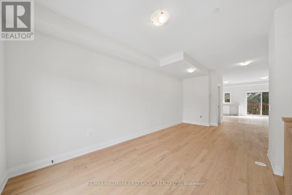 Bright white room with light wood floors, showing an open concept layout and stairs. - 11 Marret Lane, Clarington