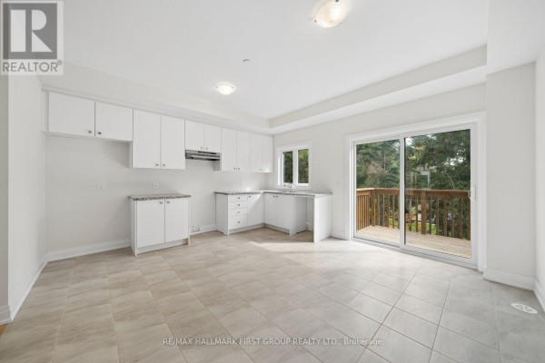 White kitchen with light tile floors, granite counters, and a sliding glass door to a wooden deck. - 11 Marret Lane, Clarington