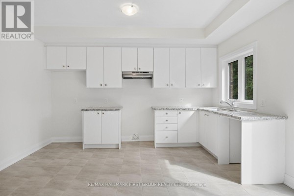 White kitchen with light tile floors, white cabinetry, granite counters, and a window with a wooded view. - 11 Marret Lane, Clarington