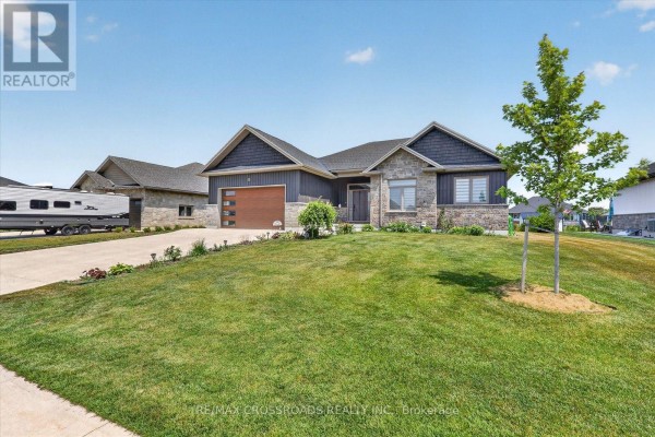 Side view of a bungalow showing the garage, driveway, lawn, and a nearby RV on the left. - 11 Mctavish Crescent, Huron Kinloss