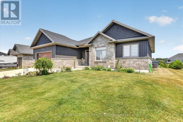 Exterior of a modern bungalow with a sloped lawn, stone and dark siding, and a covered entryway. - 11 Mctavish Crescent, Huron Kinloss