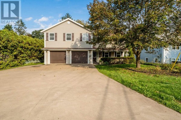 Front view of a two-story house with beige siding, two garage doors, and a paved driveway. - 11 Robie Tufts Drive, Wolfville
