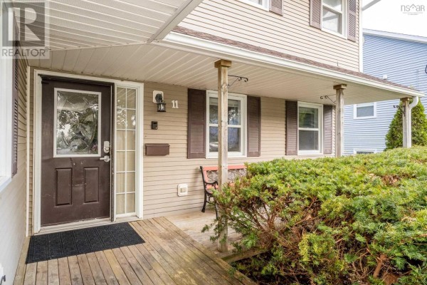 Covered wooden porch with a brown front door, windows, and a small metal bench. - 11 Robie Tufts Drive, Wolfville