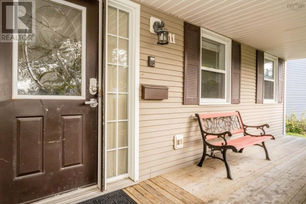 Front door and porch with wood siding, windows, a mailbox, and a metal bench. - 11 Robie Tufts Drive, Wolfville