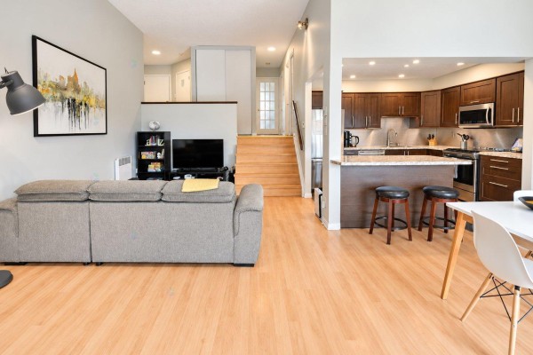 Living room with a sofa, television, stairs, and open-concept kitchen with island. - 11 Rue De Toulouse, #e, Gatineau