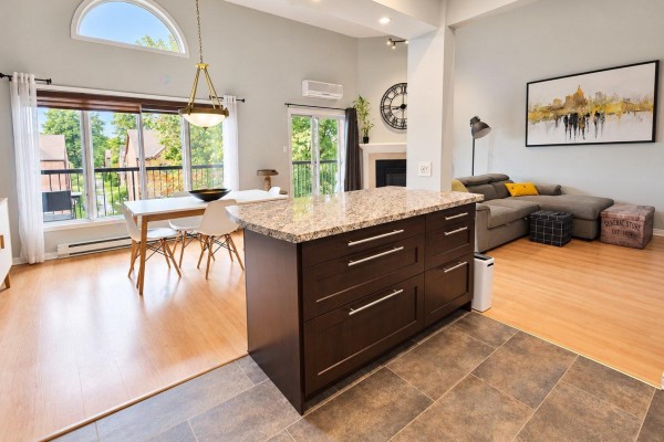 Kitchen island with granite countertop and dark wood cabinets, adjacent to living and dining areas. - 11 Rue De Toulouse, #e, Gatineau