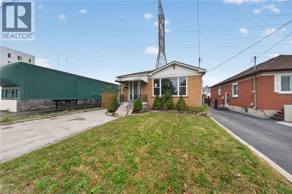 Wide exterior shot of the bungalow showing the front lawn, driveway, and neighboring house. - 11 Selkirk Avenue, Hamilton