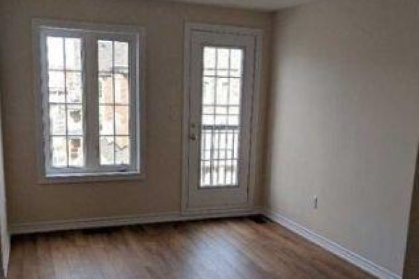 Interior room with tan walls, wood-look flooring, and a white French door with balcony. - 11 Sprucewood Road, Brampton