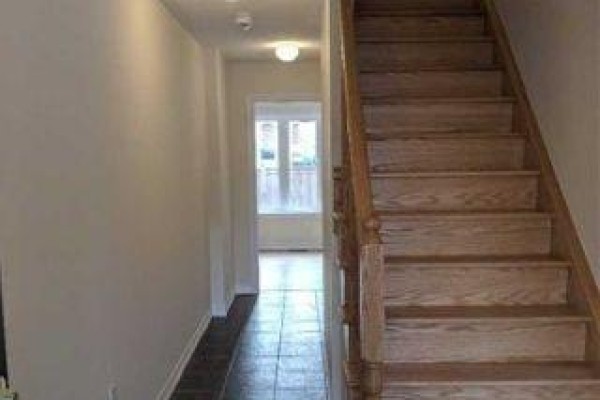 Interior hallway with tan walls, tile flooring, and a wooden staircase. - 11 Sprucewood Road, Brampton