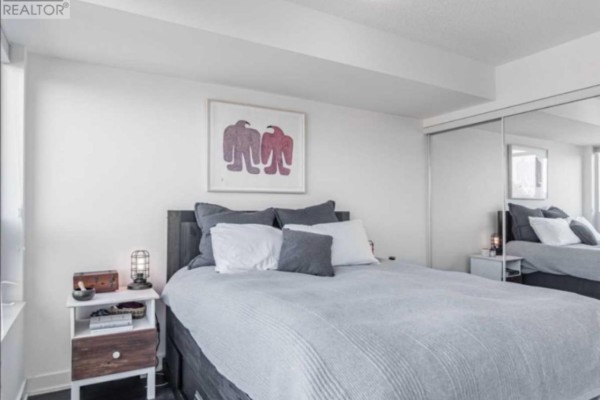 Bedroom featuring a king-size bed, grey bedding, mirrored closet doors, and a bedside table with a lamp. - 11 Superior Ave Avenue, Toronto