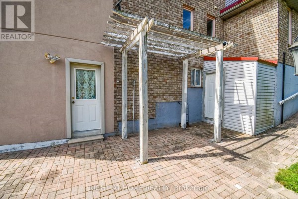 Backyard patio with brick pavers, a weathered wooden pergola, and two doors leading to the house. - 11 Thackeray Crescent, Barrie