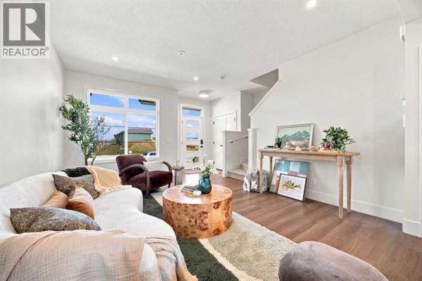 Living room looking towards the entrance, featuring white walls, hardwood floors, a sofa, chairs, and a console table. - 11 Tillotson Road, Okotoks