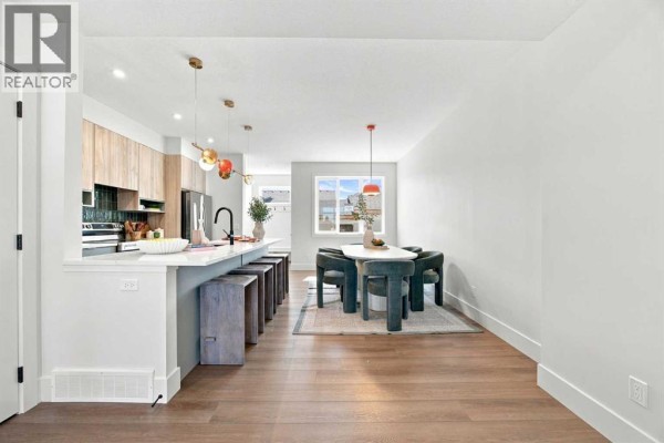 Kitchen and dining area with a white island, bar stools, light wood cabinets, a dining table with chairs, and pendant lights. - 11 Tillotson Road, Okotoks