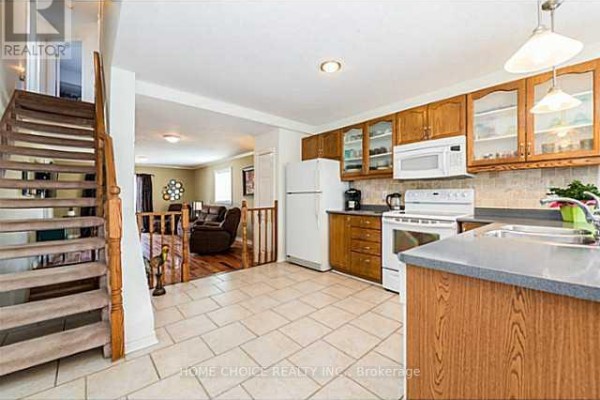 Kitchen with light tile floors, wood cabinets, white appliances, and a view of the living room. - 11 Violet Street, Barrie