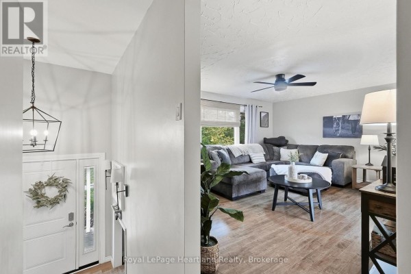 View from the entrance hall into the living room with a large sectional sofa, coffee table, and wood-look flooring. - 11 William Street N, Minto