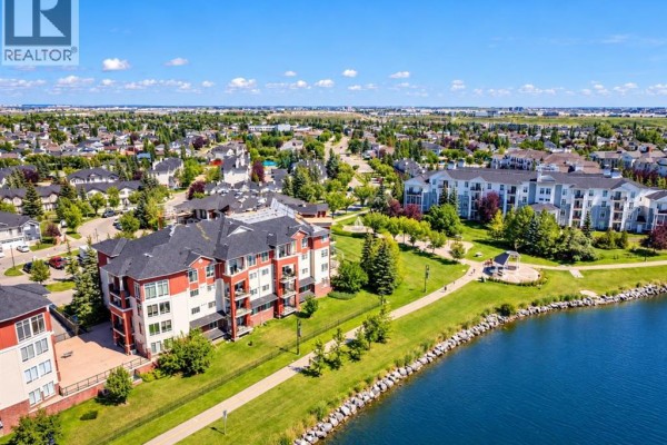Aerial view of apartment buildings next to a blue lake and green park. - 110, 162 Country Village Circle Ne, Calgary