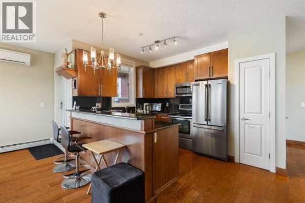 Kitchen with dark wood cabinets, stainless steel appliances, and island with bar stools. - 110, 162 Country Village Circle Ne, Calgary