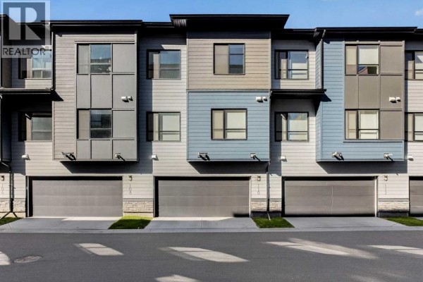 Exterior front view of a townhouse with beige and grey siding, trees, and landscaping. - 110, 42 Cranbrook Gardens Se, Calgary