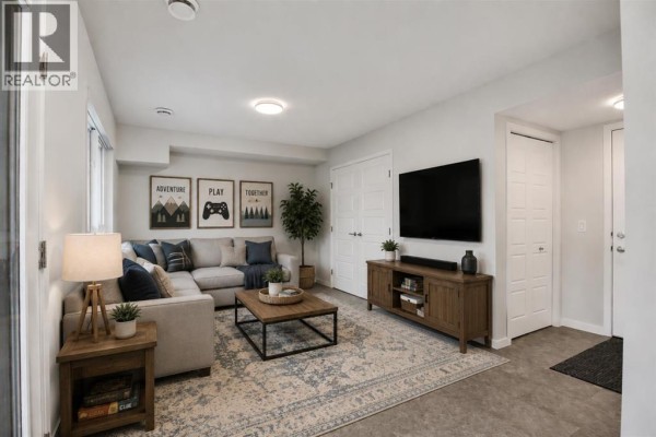 Living room with a sectional sofa, coffee table, entertainment unit, and framed wall art. - 110, 42 Cranbrook Gardens Se, Calgary