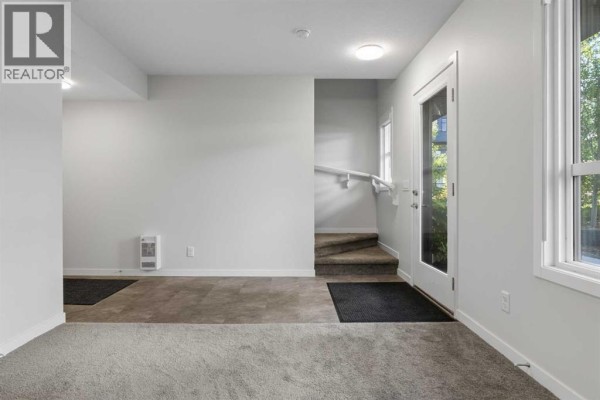 Interior hallway with light grey walls, carpet, a staircase, and a glass door. - 110, 42 Cranbrook Gardens Se, Calgary