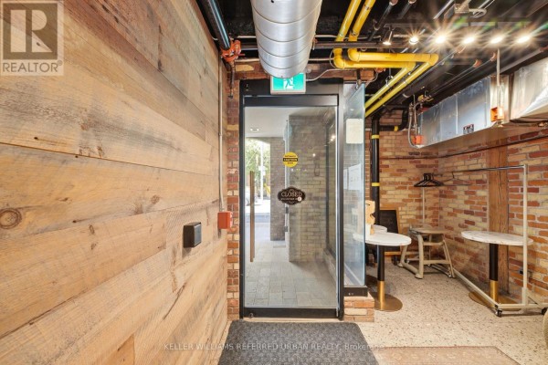 Interior view looking out the glass entrance, showing exposed brick walls and wooden paneling. - #110 - 35 Mccaul Street, Toronto