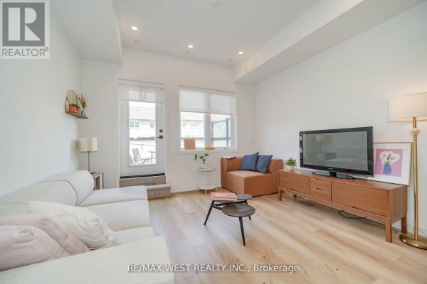 Living room with a sectional sofa, armchair, TV console, and access to an outdoor patio area. - 110 - 3686 St Clair Avenue E, Toronto