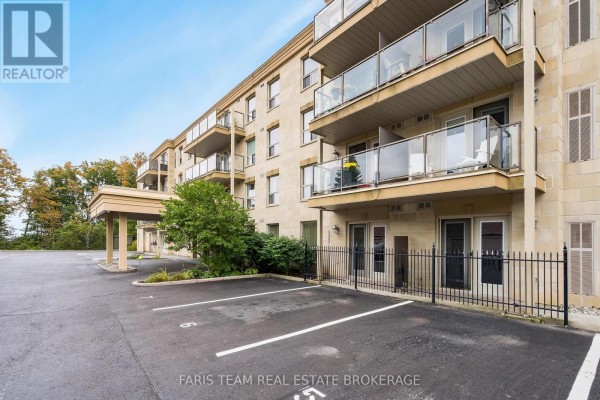 Exterior of building showing parking spots, concrete balconies with glass railings, and ground-level doors. - 110 - 486 Laclie Street, Orillia