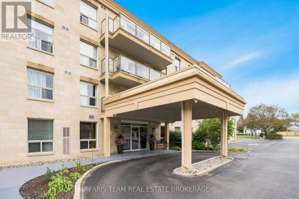 Entrance to the apartment building with a covered driveway, beige stone facade, and landscaping. - 110 - 486 Laclie Street, Orillia