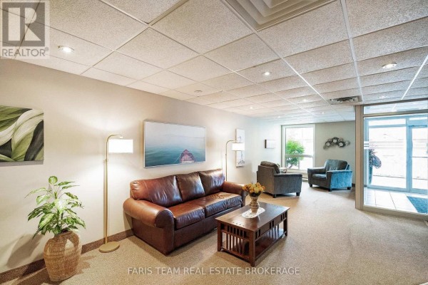 Building lobby with a brown leather sofa, armchairs, coffee table, lamps, and artwork on the wall. - 110 - 486 Laclie Street, Orillia