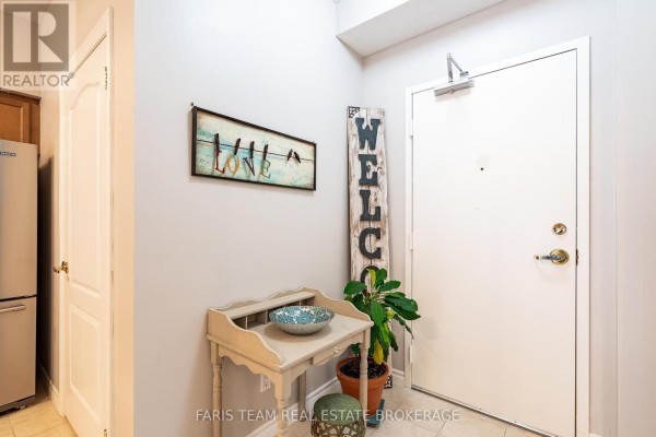 Apartment entryway with a white door, a small decorative table, plants, and wall decor. - 110 - 486 Laclie Street, Orillia