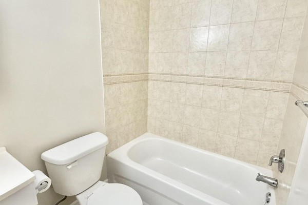 Bathroom with white bathtub, toilet, and beige tiled walls. - 110 - 55 Beechwood Place, London South